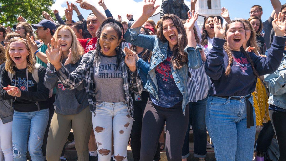 Students smiling and cheering with their hands up in front of the Saint Mary's College Chapel